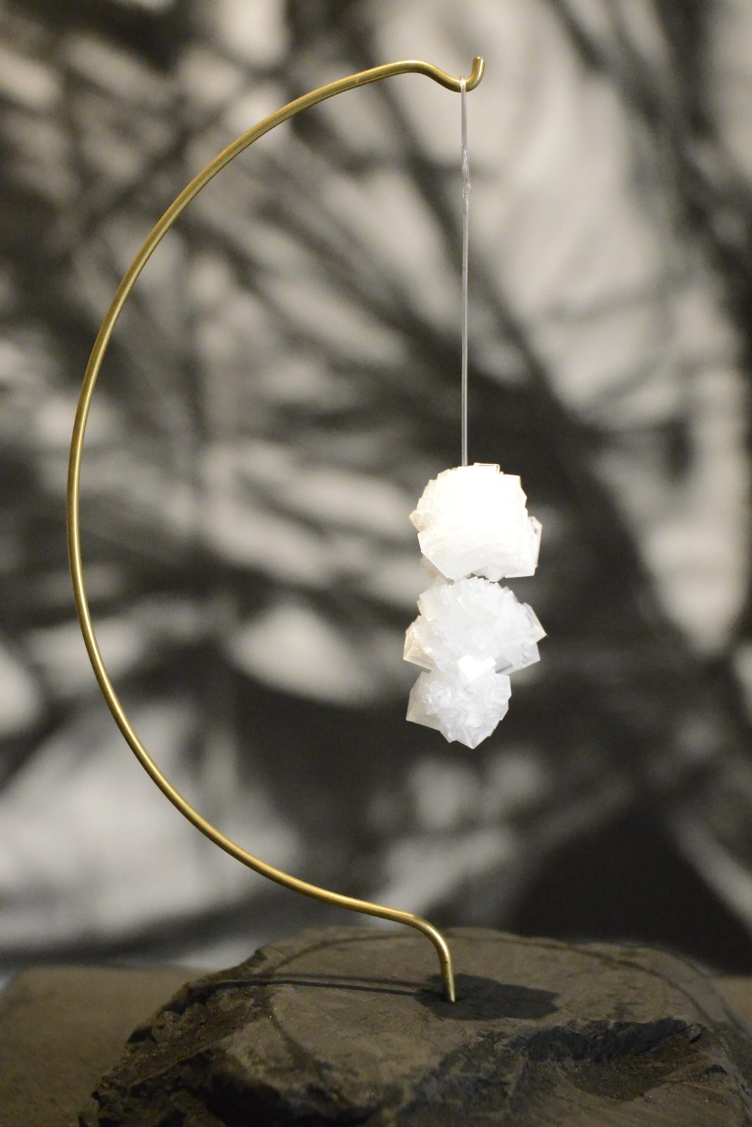where does the sadness lie, gregg bordowitz: a small white crystal hanging by a filament from a curved copper wire, over a charcoal block